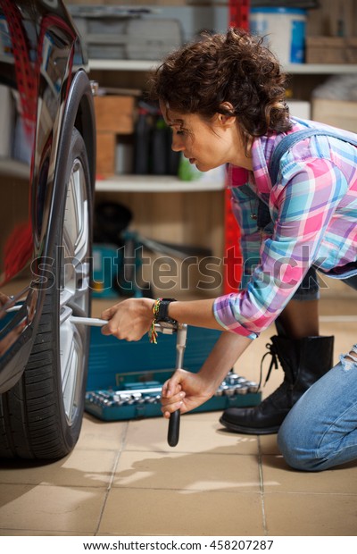 woman mechanic in overalls tighten the fixing bolts\
on the wheel of the car