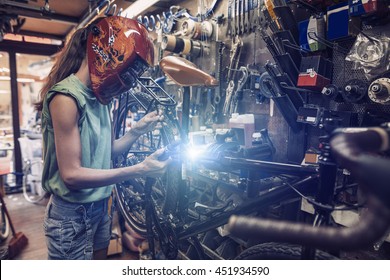 woman mechanic is repairing a bicycle using electric welding  - Powered by Shutterstock