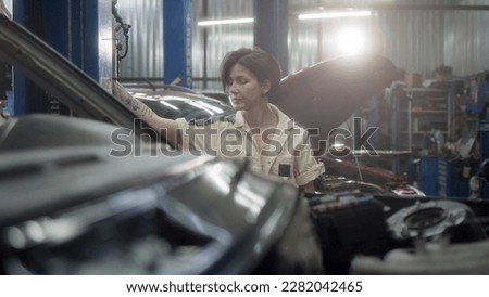 woman mechanic with tattoos lifts car on hydraulic lift in car service. car service worker is preparing to carry out repairs or maintenance of car in her small repair shop, small business.