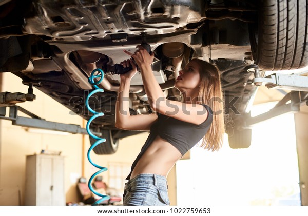 Woman mechanic tightens the bolts of the bottom of\
the car
