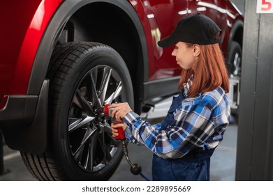 Woman mechanic uses pneumatic wrench to tighten the wheel nut. Girl at men's work.  - Powered by Shutterstock