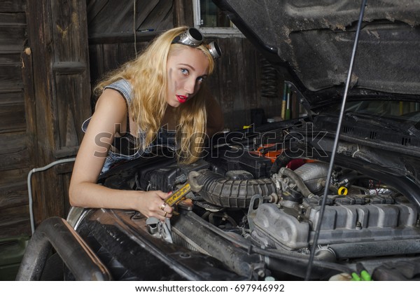 woman mechanic with a wrench looks under the hood of\
the car.