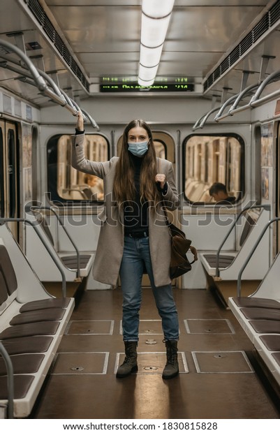 A woman in a medical face mask to avoid the spread
of coronavirus is holding onto the handrail in a subway car. A girl
with long hair in a surgical mask against COVID-19 is standing on a
metro train.