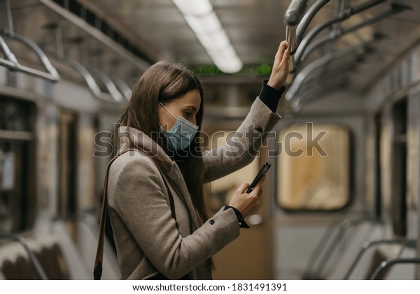 A woman in a medical face mask to avoid the spread\
of coronavirus is using a smartphone in a subway car. A girl in a\
surgical mask against COVID-19 is scrolling news on her cellphone\
on a train.