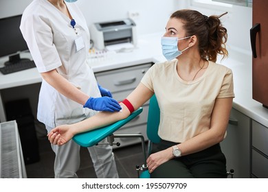 Woman in a medical mask being prepared for venipuncture