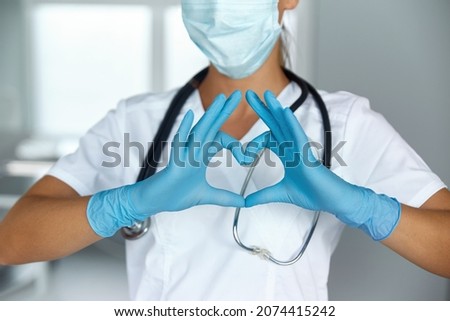 Woman with a medical mask and hands in latex glove shows the symbol of the heart. Doctor for the heart. Love our medical professionals.