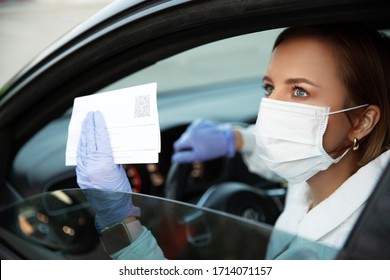 Woman In Medical Mask And Latex Gloves Sitting In Car Showing Paper Pass With QR Code For Leaving Home During Quarantine Isolation Due To Coronavirus/covid-19 Pandemic In City Lockdown