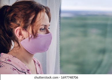 A woman in a medical mask looks out the window during a coronavirus disease. Girl in red pajamas during quarantine due to covid-19 flu virus, portrait - Shutterstock ID 1697748706