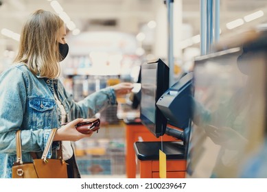 Woman in medical mask pays at self-checkouts.