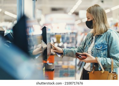 Woman in medical mask pays at self-checkouts.