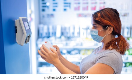 A Woman In A Medical Mask Scans The Price Of An Item In A Store. An Electronic Price Checker On The Wall In A Hypermarket