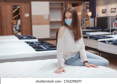 Woman In Medical Mask Shopping For New Bed During Coronavirus Quarantine, Examining Orthopedic Mattress