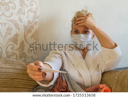 A woman in a medical mask stares wide - eyed at a thermometer. Stay at home. Stay safe. 