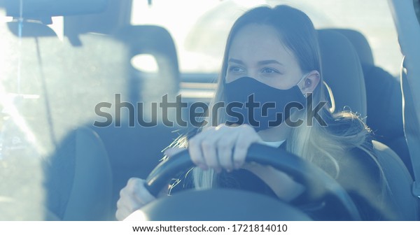 A woman\
in a medical protection mask is driving a car. The driver is\
looking in the mirrors.  Coronavirus. Covid\
-19.