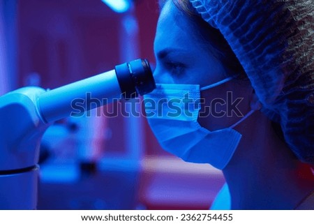Woman in a medical uniform looks through powerful microscope eyepiece