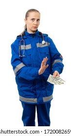 Woman In Medical Uniform And A Stethoscope. Doctor, Paramedic, Nurse Frowns, Looks At Us Seriously. An Ambulance Worker Holds Money In His Hand And Pushes Dollars Away From Him. Isolated