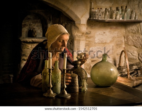 Woman\
in medieval outfit working as an alchemist or witch in the kitchen\
of a French medieval castle - with property\
release