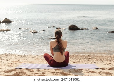 A woman meditates on the beach at sunrise, seeking relaxation and wellness through nature - Powered by Shutterstock