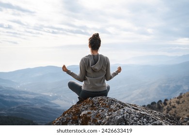 Woman meditates in yoga asana Padmasana, girl practices yoga and meditates on the mountain, back view of a yogi doing yoga in the mountain - Powered by Shutterstock