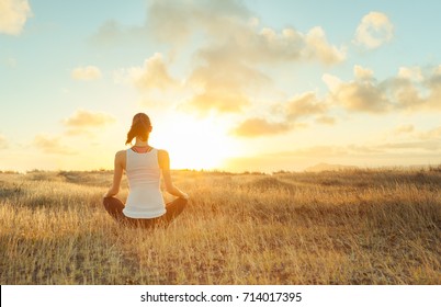 Woman meditating against a beautiful sunset. Mind body spirit.  - Shutterstock ID 714017395
