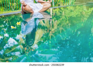 Woman meditating at pool side. Reflection in the water (focus on two floating flowers) - Powered by Shutterstock