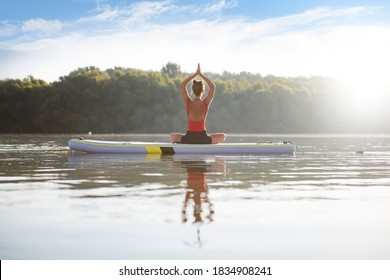 Woman meditating and practicing yoga during sunrise in paddle board