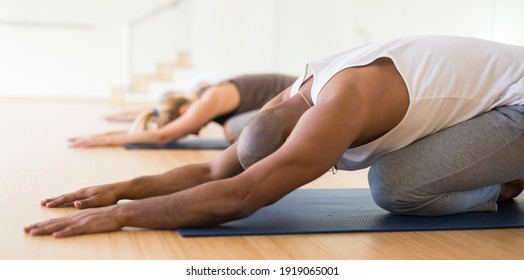 Woman And Men Performing Stretching Between Asanas During Group Yoga Training At Gym. Fitness And Hatha Yoga Concept