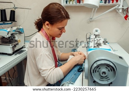 A woman mends jeans, sews a patch on a hole in the home studio.Mending clothes concept,reusing old jeans.Small business.