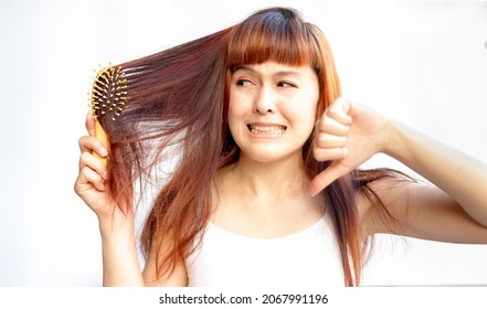 Woman With Messy Hair On A White Background. Asian Woman In Panic One Hand And Showing Thumbs Down Because Of Hair Loss. Hair With A Comb In Hand Female Having Serious Hair Fall Damaged.