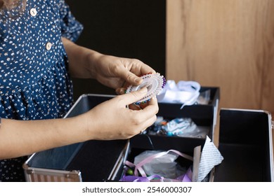 A woman meticulously organizes her sewing items, including threads and fabrics, in a home craft area, showcasing creativity and organization - Powered by Shutterstock