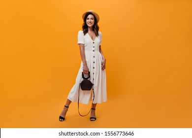 Woman In Midi Dress And Straw Hat Posing With Bag On Orange Background