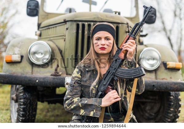 Woman in military\
uniform with rifle and\
car