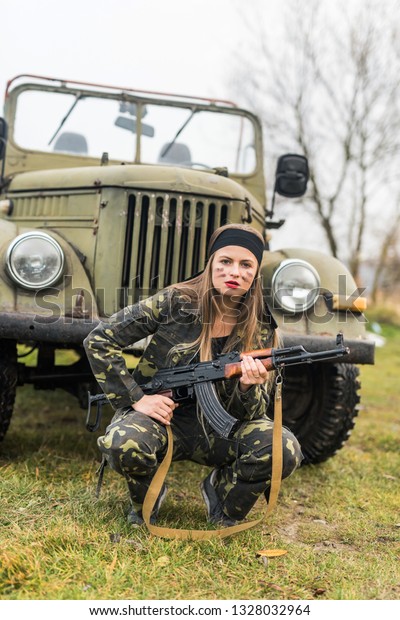 Woman in military\
uniform with rifle and\
car