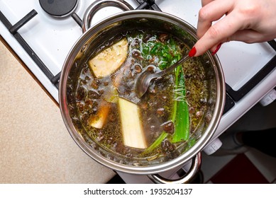The woman mixes the mushroom soup with a metal spoon which is in a metal pot on the gas stove, top view. - Shutterstock ID 1935204137