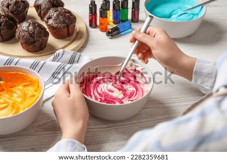 Woman mixing cream with pink food coloring at white wooden table, closeup. Decorate cupcakes