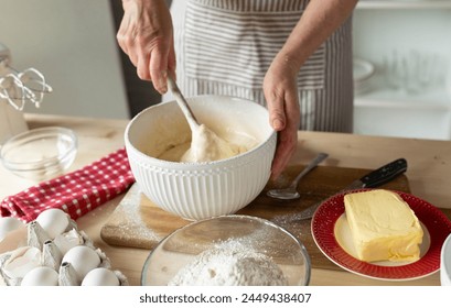 Woman mixing dough or batter with a wooden spoon in a bowl for making a cake - Powered by Shutterstock