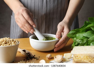 Woman Mixing Pesto Sauce With Pestle In Mortar At Table, Closeup