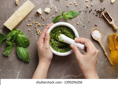 Woman Mixing Pesto Sauce With Pestle In Mortar On Grey Table, Flat Lay