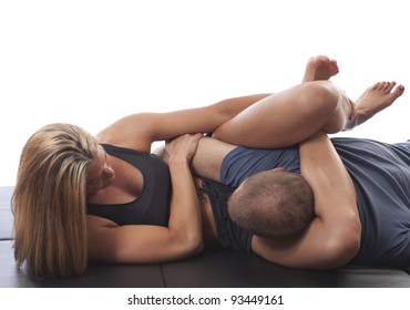 Woman in MMA attire applying a triangle choke against an opponent on black mat