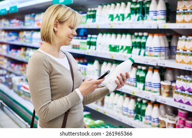 Woman With Mobile Phone Shopping Milk In Grocery Store