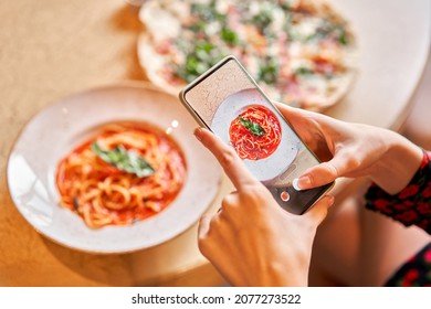 Woman with a mobile phone, takes a photo to for food blog and social networks. Italian pasta with tomato, meat. Close-up spaghetti Bolognese wind it around a fork with a spoon. Parmesan cheese
