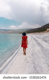 Woman Model With Her Red Dress And Hat Walking By The Lake. Turquoise Lake Salda Turkey. White Mineral Rich Beach. Salda Lake With White Sand And Green Water. Burdur Turkey