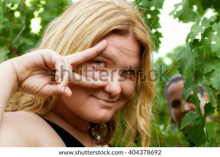 A woman models in front of grape vines while another peeks through the leaves with a big, silly grin.  The woman in the front is making a symbol that means, "fierce".