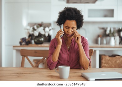 A woman in a modern kitchen interior is visibly stressed while talking on her phone, with a focused and concerned expression. The scene conveys emotions of worry and anxiety in everyday life. - Powered by Shutterstock