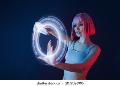 Woman in modern VR glasses interacting with network while having virtual reality experience. Augmented reality game, future technology, AI concept. VR. Holographic interface to display data. - Shutterstock ID 2079026995