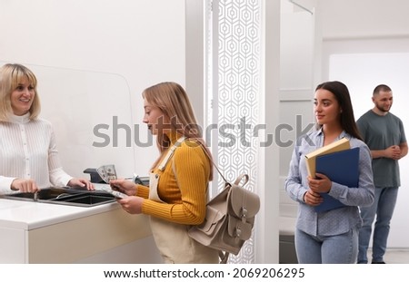 Woman with money and other people in line at cash department window. Currency exchange