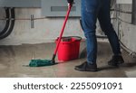 Woman mopping flood from water leaks in basement or electrical room. Water damage from rain, snowmelt or pipe burst coming from multiple cracks and leaks in concrete wall and ceiling. Selective focus.
