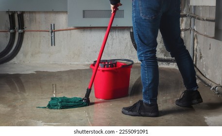 Woman mopping flood from water leaks in basement or electrical room. Water damage from rain, snowmelt or pipe burst coming from multiple cracks and leaks in concrete wall and ceiling. Selective focus.