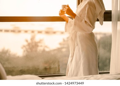 Woman In The Morning.Women Wake Up Early With Coffee In Bathing Suits.Woman In The Morning With Coffee And Looking At The Sunrise Standing Near The Window