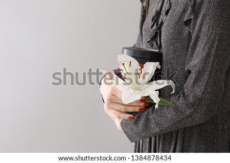 Woman with mortuary urn and lily flower on light background